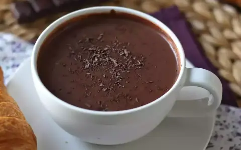 En vit mugg med varm choklad, toppad med chokladspån. En croissant ligger bredvid.