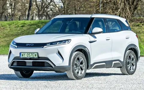 Biały SUV z logo BYD, jeden z chińskich samochodów elektrycznych, zaparkowany na żwirowej nawierzchni.