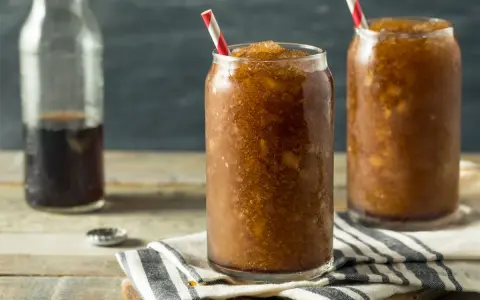 Zwei Gläser mit erfrischendem Cola Slush Eis, bereit zum Genießen. Eine Flasche Cola steht daneben.