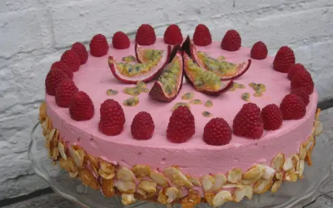 En rosa hallonmousse tårta dekorerad med färska hallon och passionsfrukt. Kanterna är täckta med rostade mandelflagor.