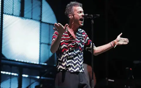 El cantante de Vetusta Morla Sevilla canta apasionadamente en un concierto, con las manos extendidas y un micrófono frente a él.