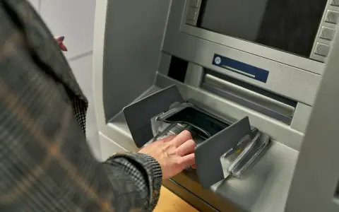 Dłoń w rękawie w kratę wkłada pieniądze do bankomatu. Szybka jednorazowa wpłata gotówki do banku.