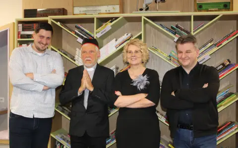 Jacek Ostrowski z książkami w kolejności. Grupa osób pozuje na tle regałów z książkami.