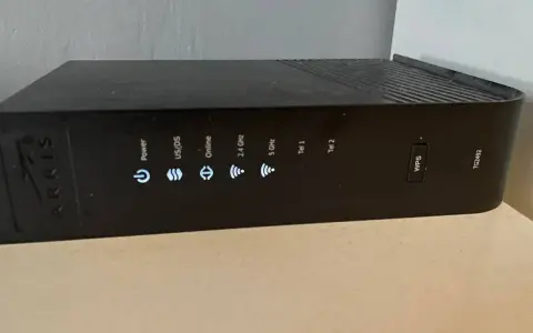 Czarny router Arris TG2492 z widocznym przyciskiem WPS i wskaźnikami stanu: Power, US/DS, Online, 2.4 GHz, 5 GHz, Tel 1, Tel 2.