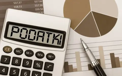 Kalkulator z napisem "PODATKI" obok wykresów i długopisu. Obliczenia podatku od sprzedaży działki.