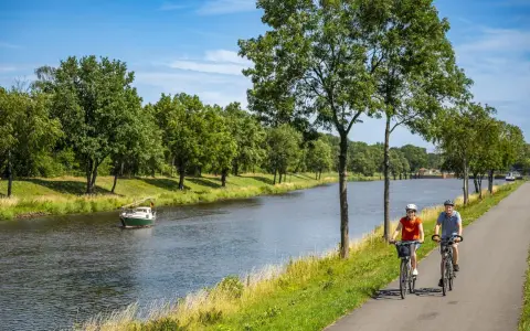 Zwei Radfahrer genießen eine Tour auf dem Dortmund-Ems-Kanal-Radweg. Ein kleines Boot fährt auf dem Wasser.