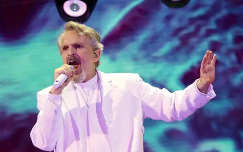 Un hombre con traje blanco canta en un escenario con luces vibrantes. ¡Murcia on!