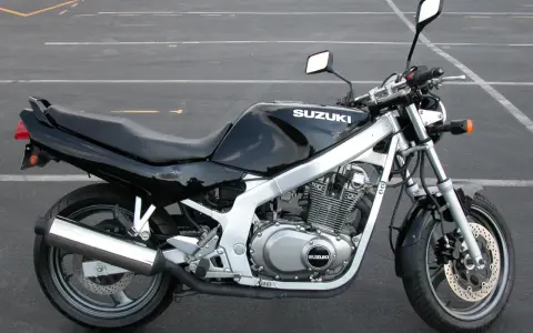 Czarny motocykl Suzuki GS 500 z chromowanym wydechem stoi na pustym parkingu.