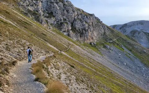 Due escursionisti percorrono un sentiero di trekking sul Gran Sasso, tra rocce e vegetazione alpina.