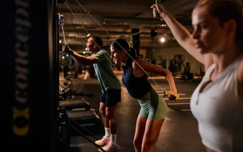 Drei Personen machen ein intensives AMRAP Workout an Kabelzügen. Sie ziehen die Griffe nach hinten und trainieren so ihren Rücken.