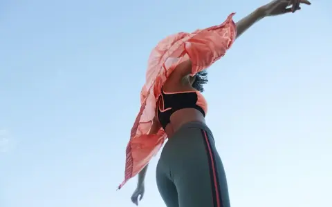 Kobieta w sportowym stroju, w tym legginsach z materiału spandex, tańczy na tle błękitnego nieba.