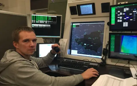 Młody kontroler ruchu lotniczego w wieku około 30 lat pracuje przy konsoli z wieloma monitorami wyświetlającymi mapy lotnicze i dane.
