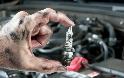 A mechanic's greasy hand holds a used spark plug, a reminder that many cars still have spark plugs for ignition.