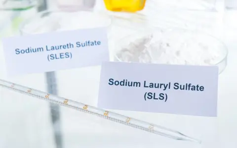 Białe proszki w naczyniach laboratoryjnych, jeden z etykietą "Sodium Laureth Sulfate (SLES)", obok pipeta.