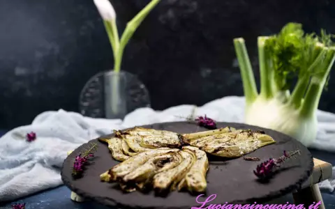 Finocchi croccanti e dorati, cotti nella friggitrice ad aria, serviti su una pietra scura con erbe aromatiche.