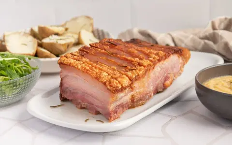 Panceta de cerdo al horno con piel crujiente, acompañada de patatas asadas y ensalada.