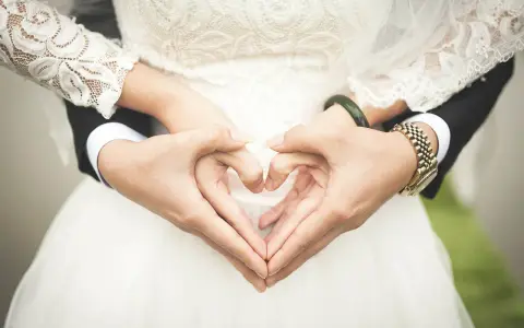 Manos formando un corazón, celebrando 2 años de casados. Vestido de novia blanco y traje negro.