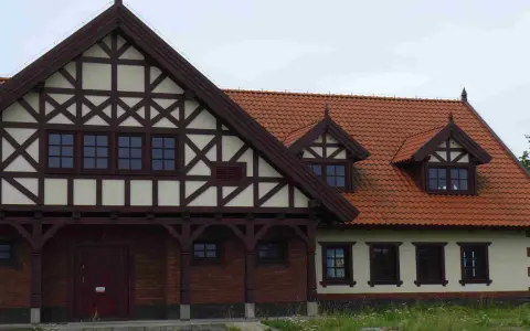 Elewacja budynku w stylu mur pruski, z charakterystyczną drewnianą szachownicą na jasnym tle i ceglanym parterem.