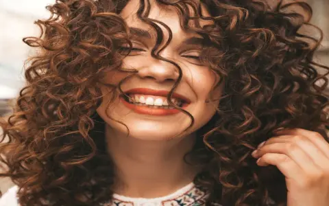 Mujer sonriendo con unos cortes de pelo rizado espectaculares, su cabello castaño cae en cascada alrededor de su rostro.