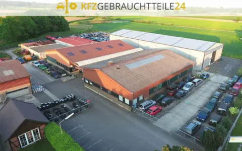 Luftaufnahme eines Autoteile-Lagers mit Gebäuden und vielen Autos.
