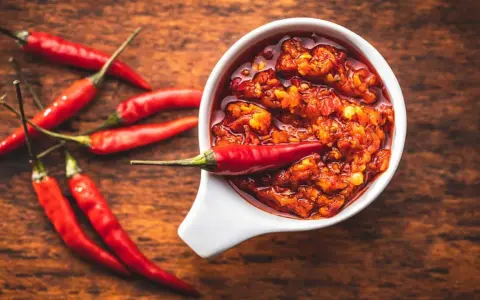 Scharfes Essen stillen: Eine Schale mit feuriger Chilisauce und frischen roten Chilis auf einem Holztisch.