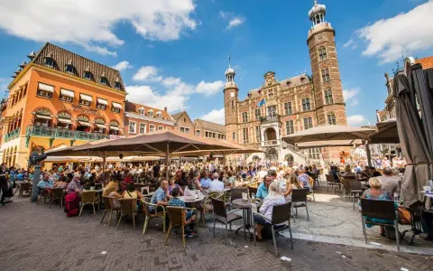 Lebhafter venlo markt mit vielen Menschen, die in Cafés unter Sonnenschirmen sitzen. Im Hintergrund das historische Rathaus.