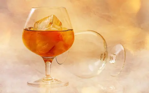 Kieliszek z bursztynowym płynem i lodem, obok pusty, przewrócony kieliszek. Idealny sposób, jak pić brandy.