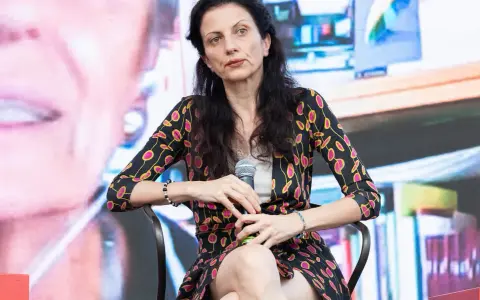 Veronica Tomassini, la cui età non è specificata, con un microfono in mano, indossa una giacca con fantasia floreale.
