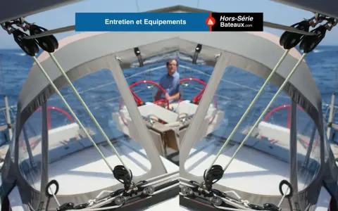 Vue depuis le cockpit d'un voilier, avec un homme au gouvernail. Les cordages et poulies sont visibles, prêts pour une navigation. L'équipement VHF ASN est essentiel pour la sécurité.