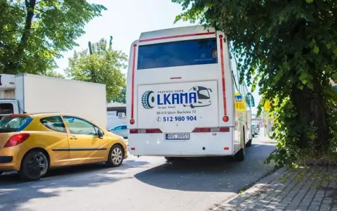 Autobus LKAMA z napisem "Voyager Nowy Sącz Gorlice" stoi obok żółtego samochodu.