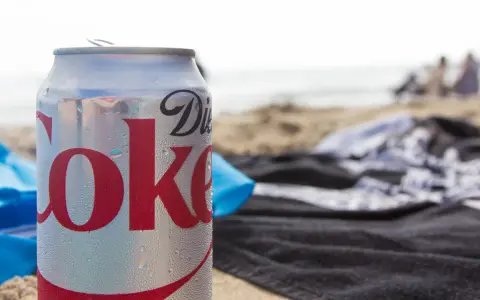 En burk Diet Coke på stranden, perfekt för den som vill undvika socker och hantera diabetes. Sukralos i drycken gör den till ett sockerfritt alternativ.