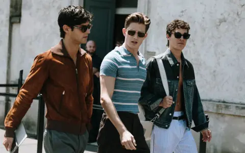 Tre uomini camminano insieme, uno con giacca marrone, uno con polo a righe e uno con giacca di jeans. Un look uomo di stile.
