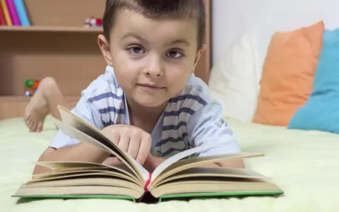 Chłopiec leży na łóżku z otwartą książką. To świetny sposób, jak zachęcić dziecko do czytania.
