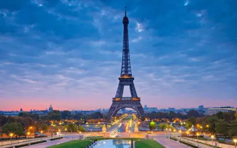 Torre Eiffel iluminada al atardecer, uno de los iconos franceses más reconocidos, con el cielo azul y nubes rosadas.