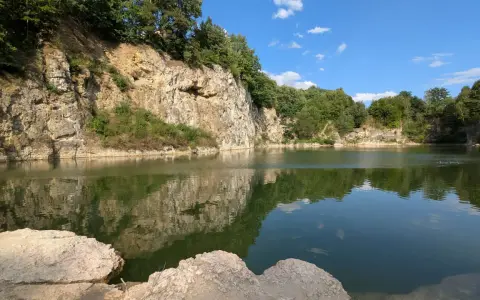 Spokojny zalew kamieniołom w Zabierzowie, z odbijającymi się w wodzie skalnymi ścianami i zielenią drzew.