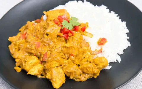 Pyszny kurczak curry fit z ryżem, papryką i kolendrą na czarnym talerzu. Idealny posiłek dla dbających o linię.