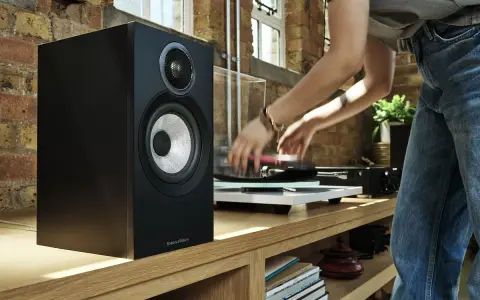Czarny głośnik Bowers & Wilkins, jeden z najlepszych producentów głośników, obok gramofonu, na którym osoba kładzie płytę.