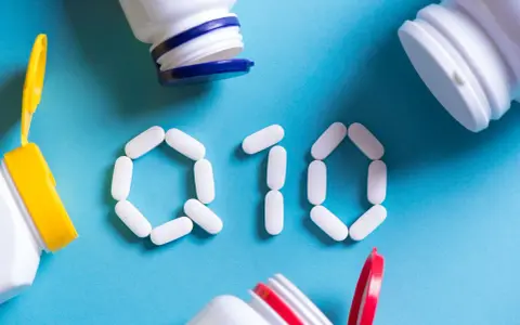 Białe tabletki ułożone w kształt "Q10" na niebieskim tle, obok otwarte pojemniki z suplementami. Koenzym Q10 na co?