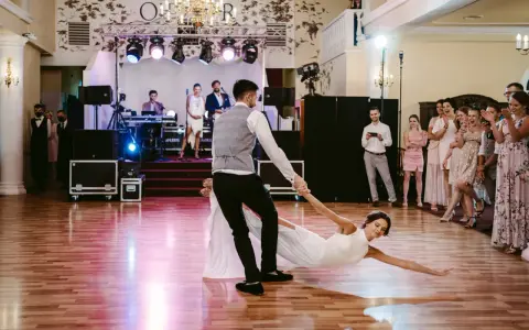 Para młoda wykonuje widowiskowe podnoszenia w tańcu, goście z zachwytem obserwują ich występ.