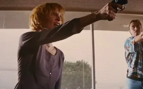 Donna e uomo puntano pistole, in una scena che ricorda un cliffhanger traduzione.