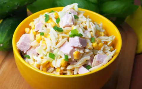 Pyszna sałatka z makaronem orzo, kawałkami szynki, kukurydzą i szczypiorkiem, podana w żółtej misce.
