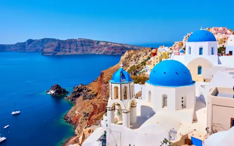 Santorini wakacje: białe domy z niebieskimi kopułami na tle turkusowego morza i klifów. Idealne miejsce na wymarzone wakacje.