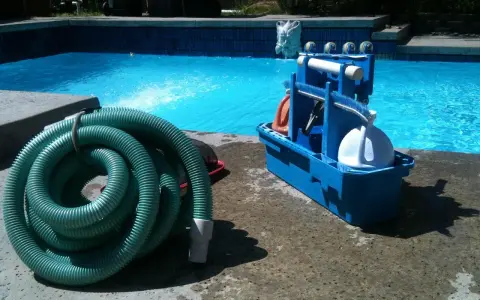 Tuyau vert enroulé et boîte bleue d'accessoires de nettoyage pour le branchement piscine.