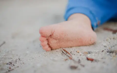 Mała stópka rocznego dziecka w piasku. Takie odkrycia to radość, gdy dziecko zaczyna chodzić po domu i odkrywać świat.