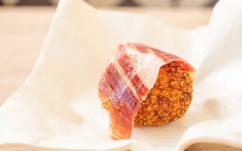 Croqueta dorada con jamón ibérico, servida sobre papel blanco.
