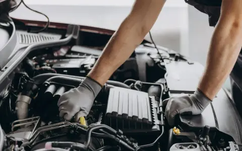Mechanik w rękawiczkach pracuje przy silniku, dbając o zgodność z normami emisji spalin i tabelą CO2.