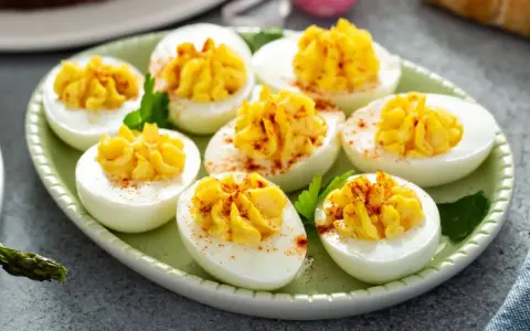 Oeufs mimosa au thon, garniture jaune crémeuse saupoudrée de paprika sur des blancs d'œufs sur une assiette verte.