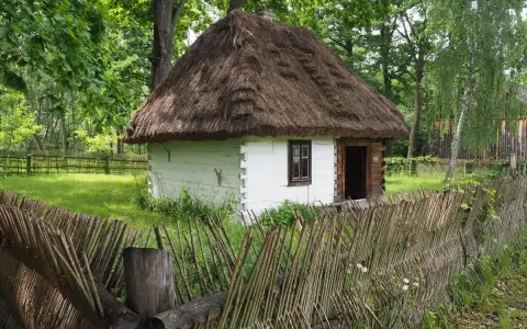 Drewniana chata z krytym strzechą dachem i płotem z gałęzi. Wspaniałe radom atrakcje, które przenoszą w przeszłość.