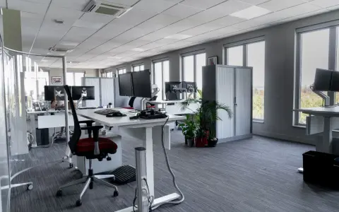 Aménagement moderne de bureaux en open space avec postes de travail équipés de plusieurs écrans, chaises ergonomiques et rangements.