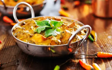 Ein cremiges Curry, garniert mit Koriander, umgeben von bunten Chilis. Ein Genuss für Liebhaber indischer Gerichte.